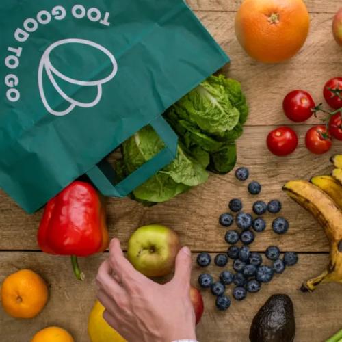 a person is holding a bag of fruits and vegetables on a wooden table .