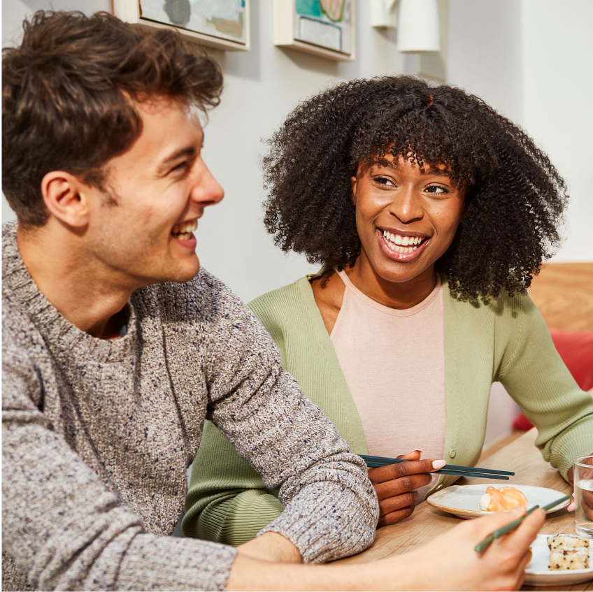 a man and a woman are sitting at a table with plates of food and chopsticks