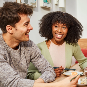 a man and a woman are sitting at a table with plates of food and chopsticks