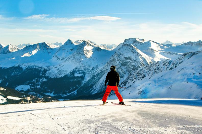 a person is standing on top of a snow covered mountain looking at the mountains .