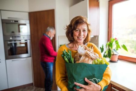 a woman is holding a bag of groceries in a kitchen .