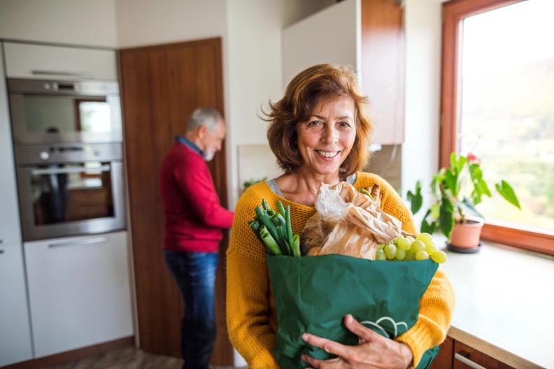 a woman is holding a bag of groceries in a kitchen .