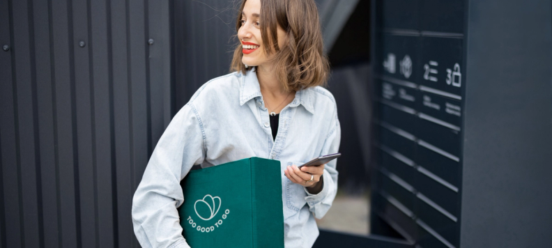 Happy Woman holding a Too Good To Go branded box and her phone