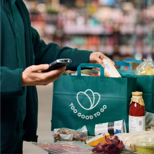 a man is looking at his phone while holding a bag that says too good to go