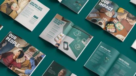 Multiple open Too Good To Go brochures displaying articles about food waste, arranged on a teal surface.