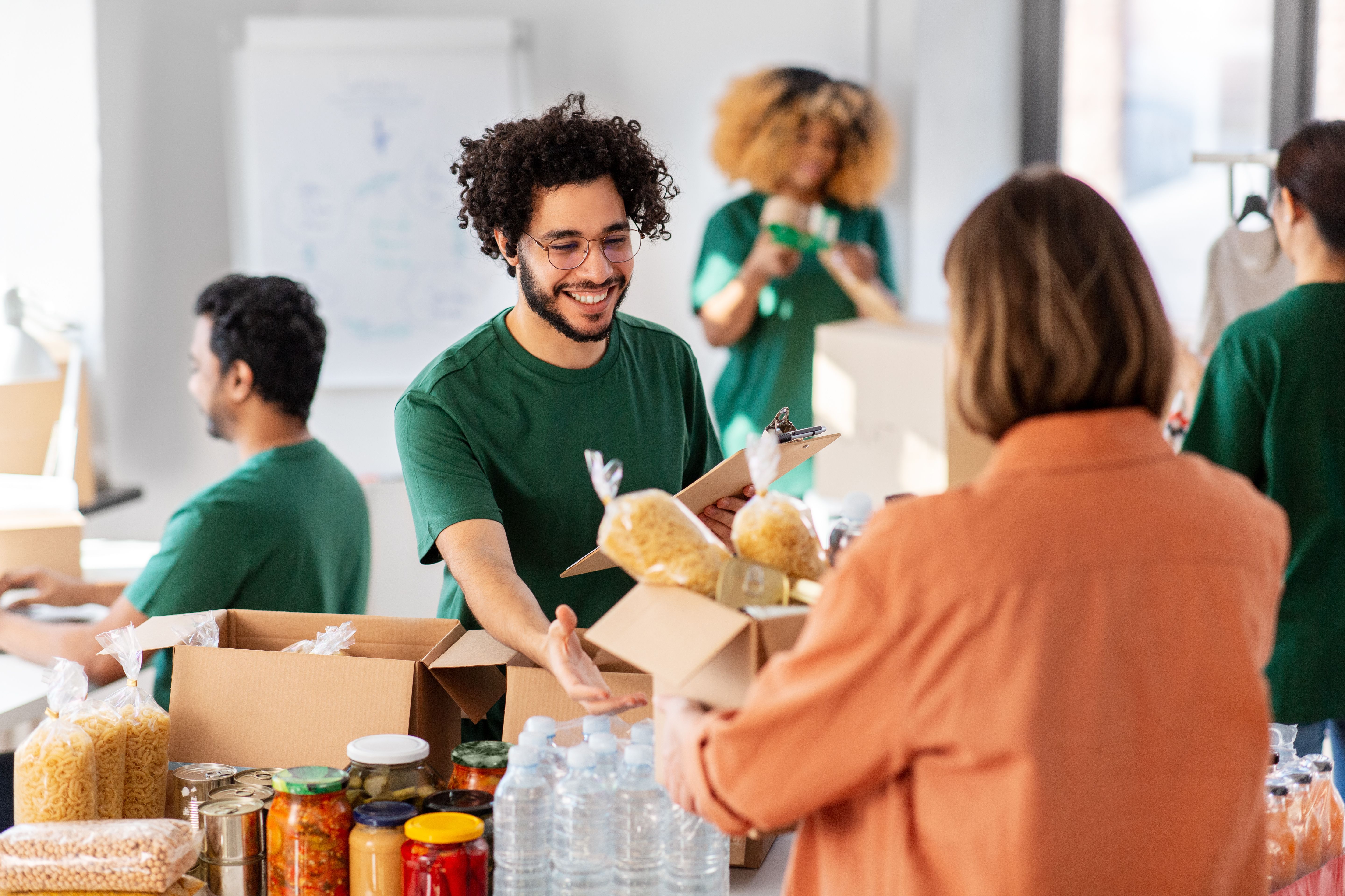 Smiling volunteer hands food donations to a person at a busy charity event.