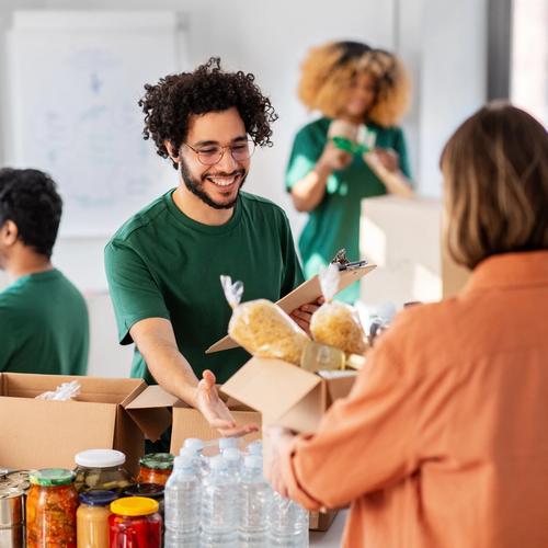 Smiling volunteer hands food donations to a person at a busy charity event.