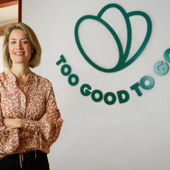 a woman stands in front of a sign that says too good to go