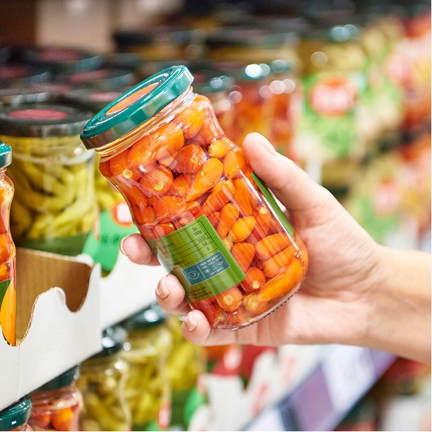 a person is holding a jar of pickles in a grocery store .