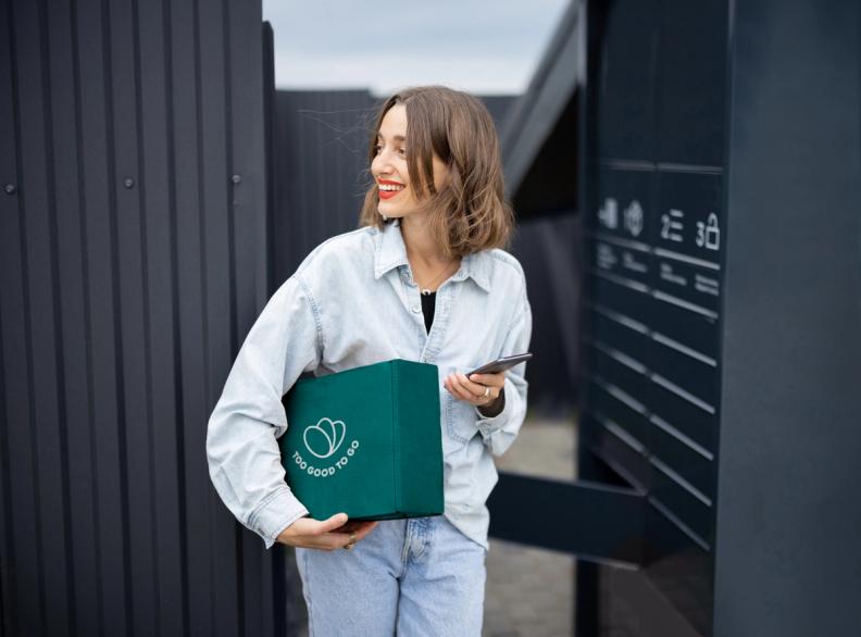 a woman is holding a green box and a cell phone .
