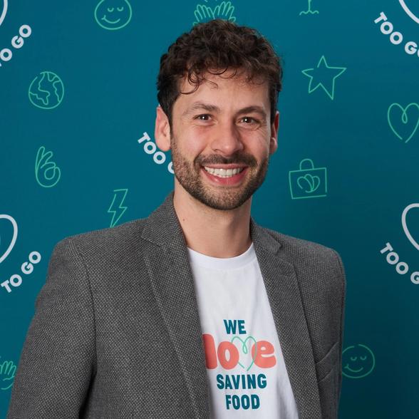 a man wearing a suit and a t-shirt that says `` we love saving food '' is smiling .