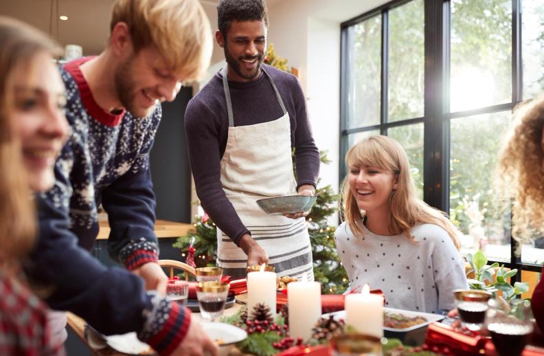 a man is serving food to a group of people at a christmas dinner table .