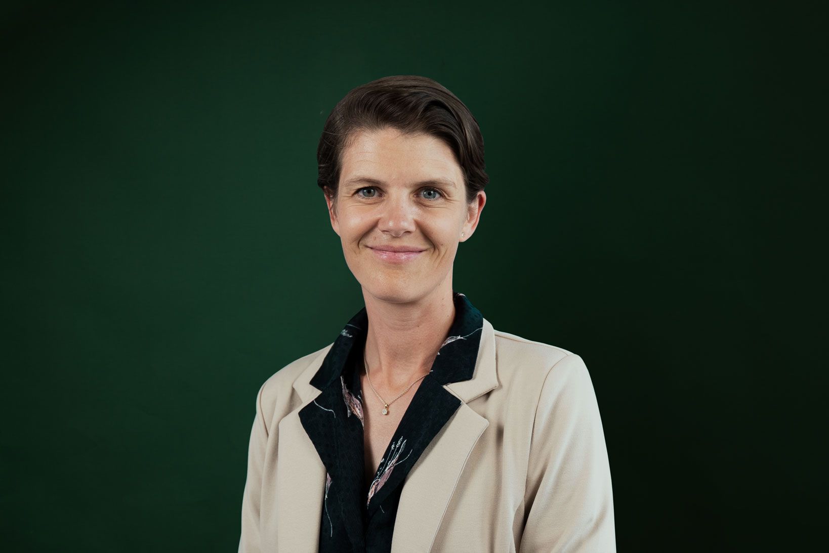 a woman in a tan jacket is smiling in front of a green background .