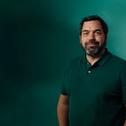 a man with a beard wearing a green polo shirt is standing in front of a green wall .