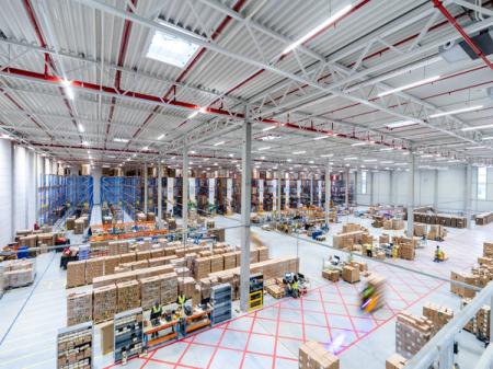 Modern, active warehouse with stacks of boxes, tall racks, and blurred workers.
