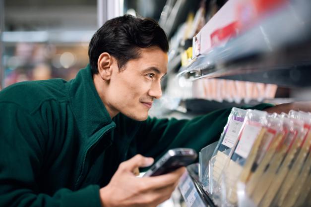 a man is looking at a cell phone in a grocery store .