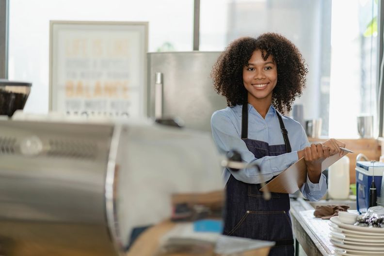 Employee working behind the counter at a cafe, carrying a clipboard.