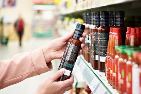 a person is holding a bottle of hot sauce in a supermarket .