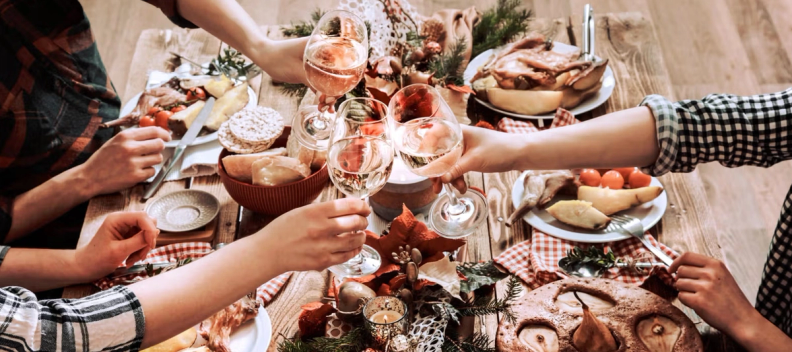 Overhead view of a festive dining table set with a greenery centerpiece, lit candles, multiple food dishes, and place settings.
