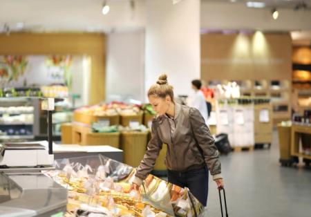 A young woman selects items from a refrigerated display case in a grocery store.
