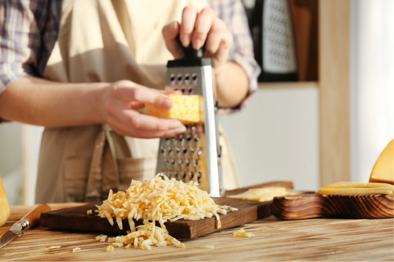 a person grating cheese on a wooden cutting board