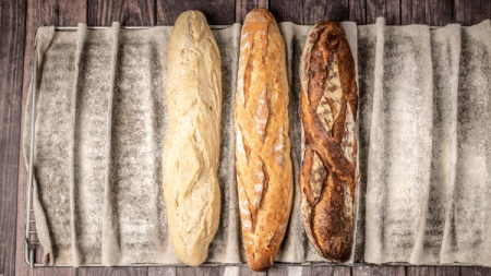 Three baguettes, light to dark, on a floured proofing cloth.