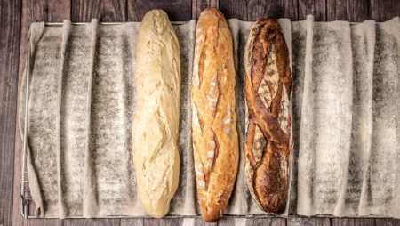 Three baguettes, light to dark, on a floured proofing cloth.