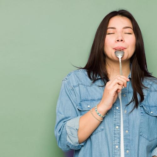 a woman is holding a spoon in her mouth with her eyes closed .