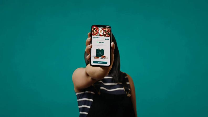 a woman holing a phone in her hand displaying a bag of Too Good To Go
