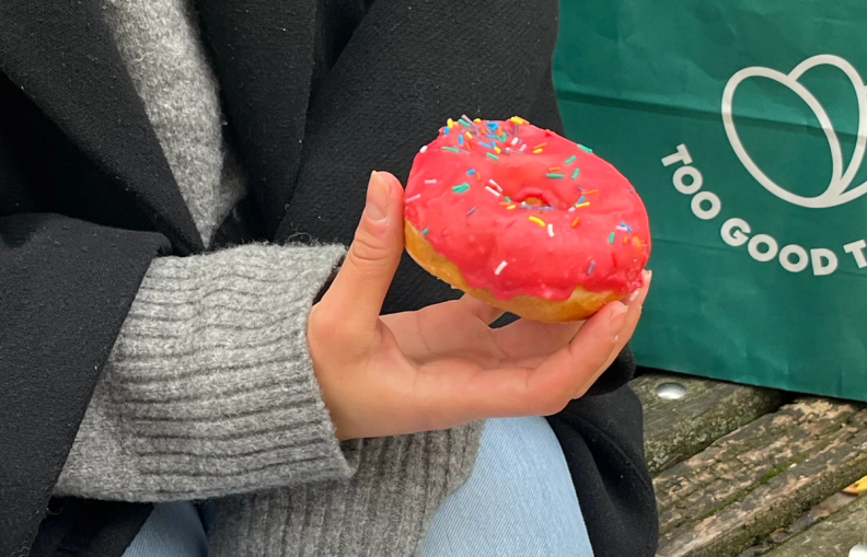 a person holding a donut in front of a bag that says too good