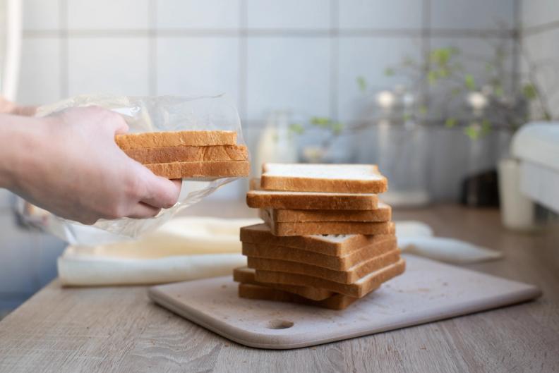 a person is putting slices of bread in a plastic bag on a cutting board .