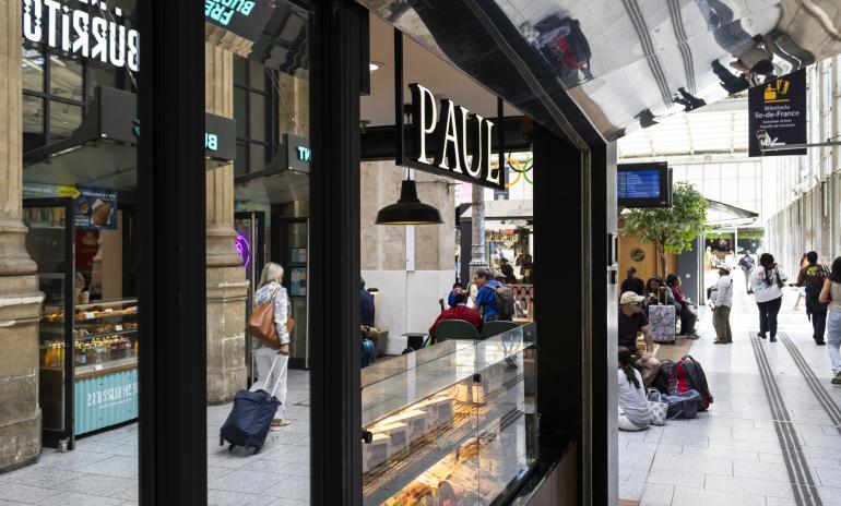 a woman with a suitcase is walking past a bakery in a train station .