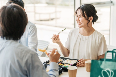 A smiling woman eats a bento box lunch with colleagues.
