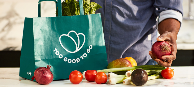 a person holding an apple next to a bag that says too good to go