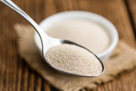 A spoon filled with yeast next to a bowl of yeast on a wooden table.
