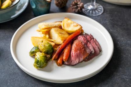 a white plate topped with roast beef , potatoes , carrots and brussels sprouts .