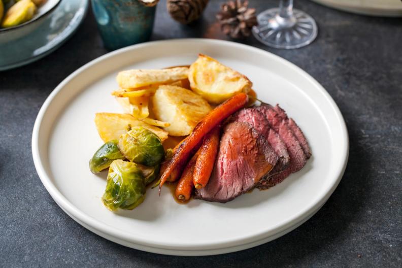 a white plate topped with roast beef , potatoes , carrots and brussels sprouts .