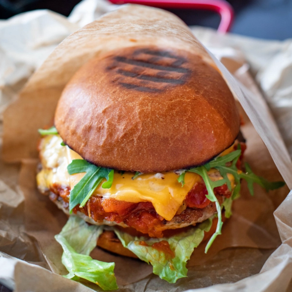 Close up of a burger with cheese and salad seeping out of it