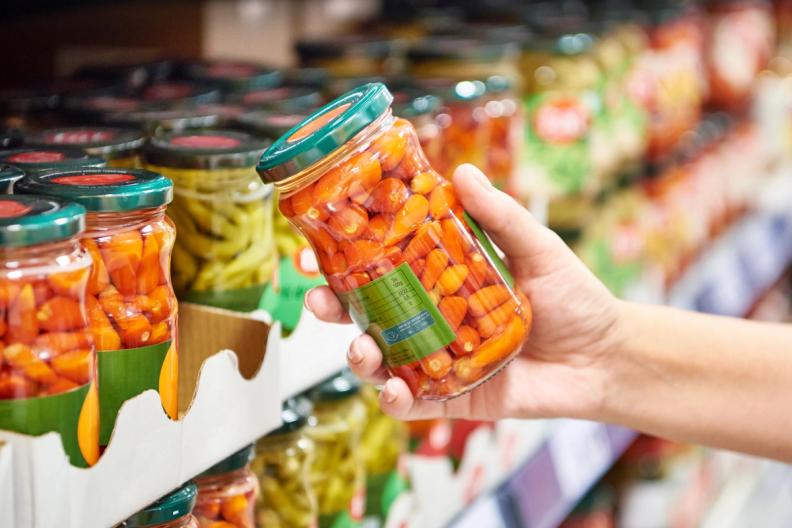 a person is holding a jar of pickles in a grocery store .