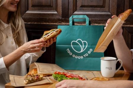 a man and a woman are sitting at a table eating sandwiches and drinking coffee .