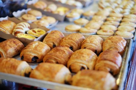 Trays of golden-brown pain au chocolat and other pastries in a bakery display.