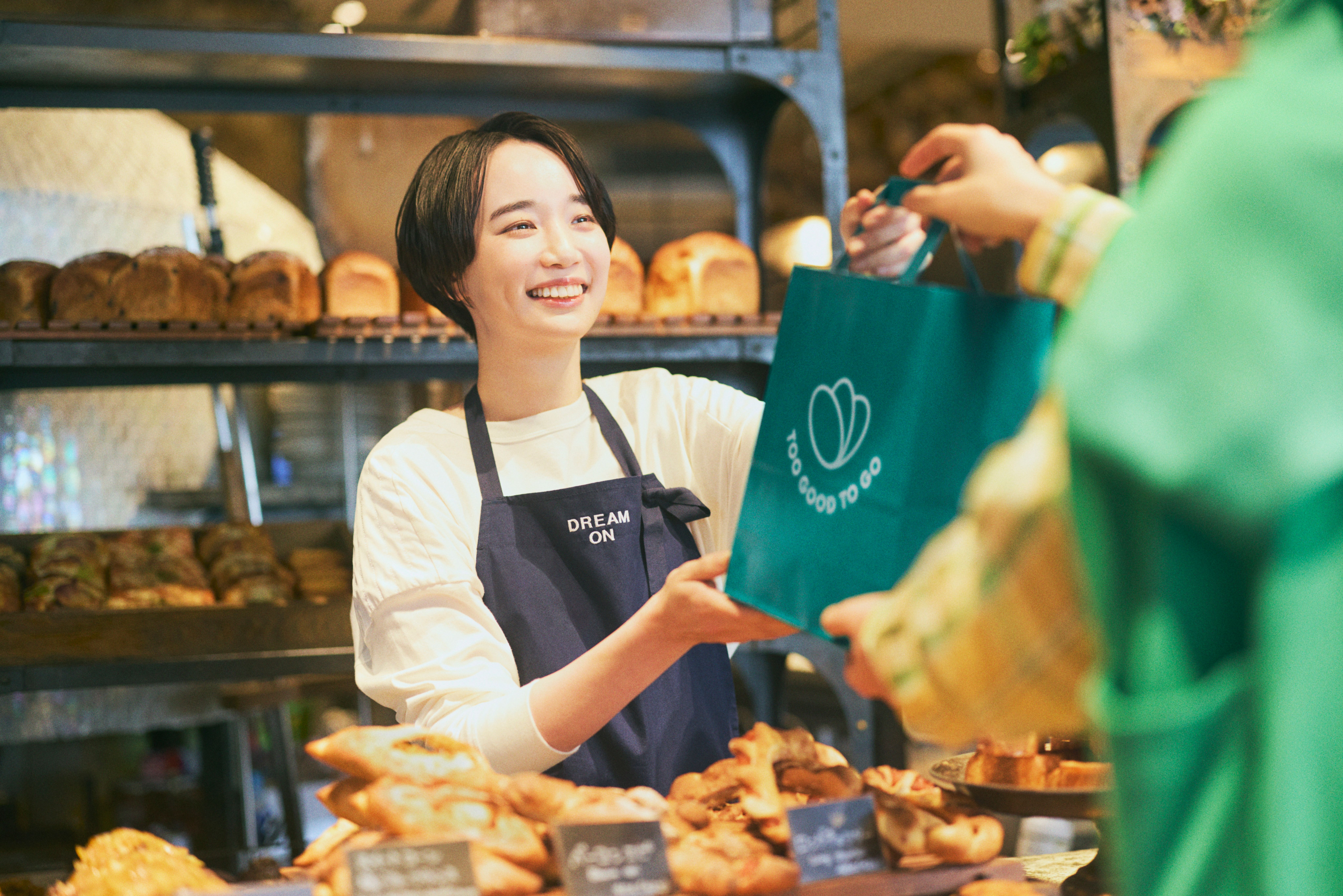 a woman using a tablet next to a bag that says too good to go