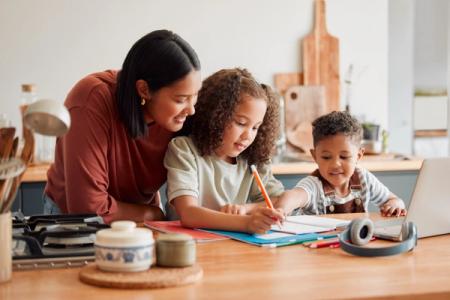 a woman is helping two children with their homework in the kitchen .