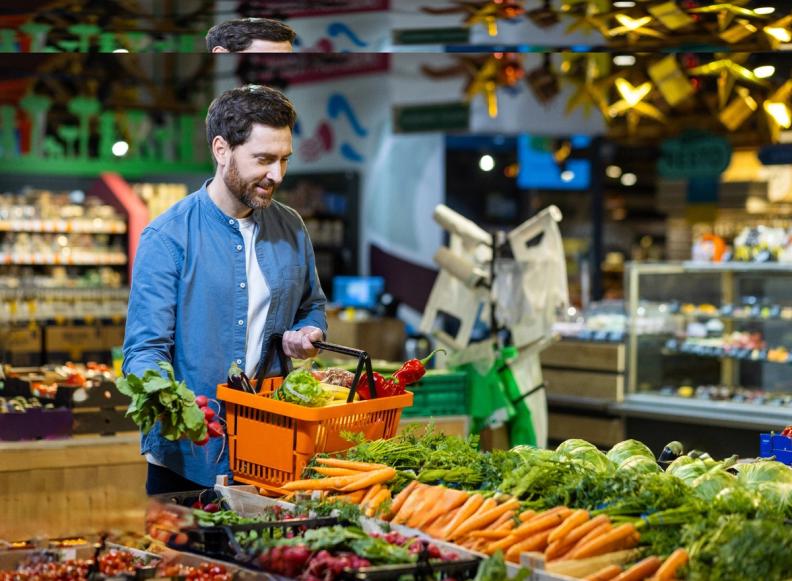 A man smiling while adding produce to an orange shopping basket in a grocery store.