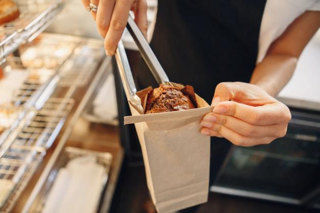 a woman is holding a bag of food with tongs in a bakery .
