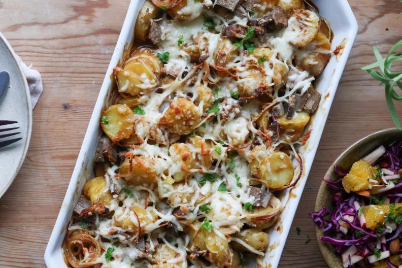 a casserole dish filled with potatoes , meat and cheese on a wooden table .