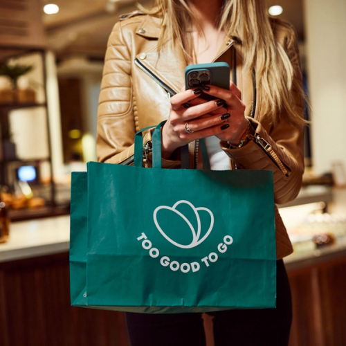 Woman torso holding phone and Too Good To Go branded bag