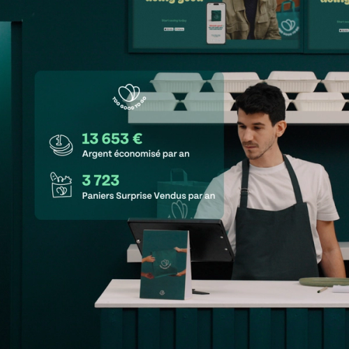 a man in an apron stands at a counter in front of a screen that says 13653 euros