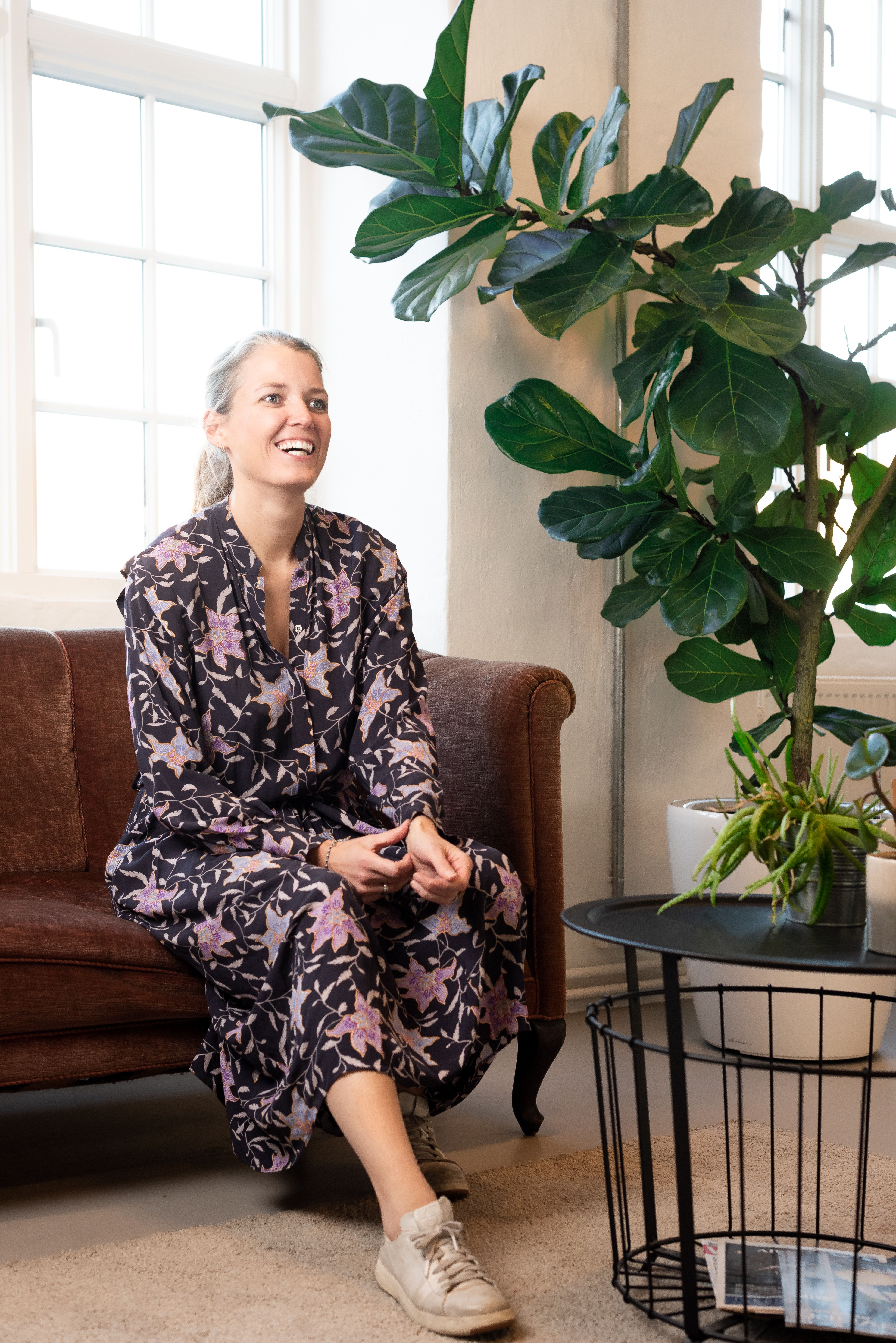 a woman sits on a couch next to a plant