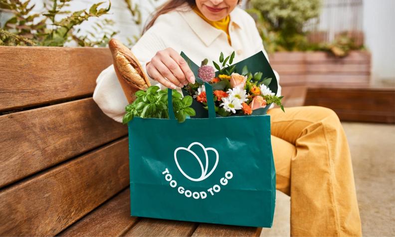 a woman is sitting on a bench holding a bag of flowers and bread .